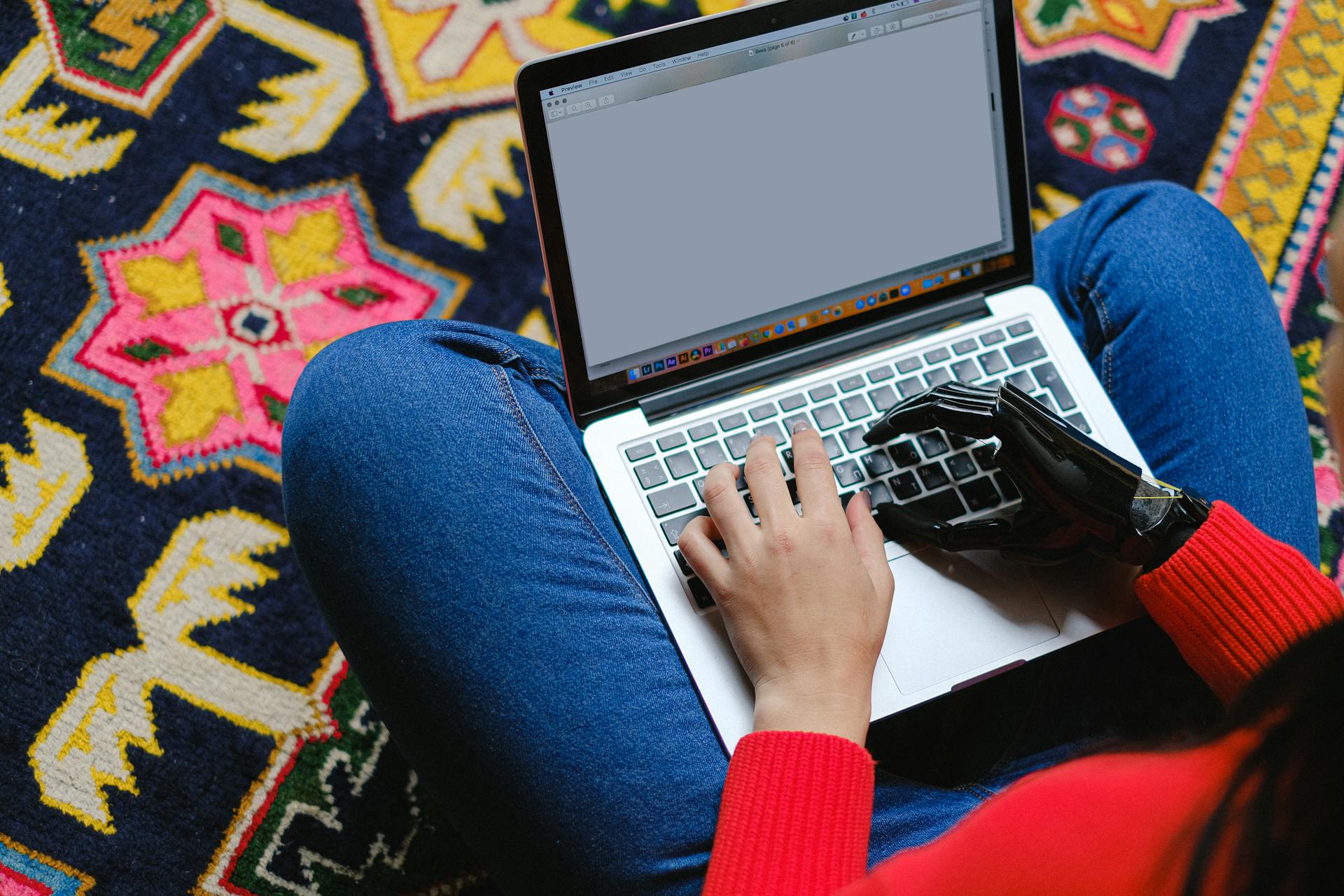 Accessibilité numérique : une personne avec une prothèse de main pianote sur un ordinateur portable posé sur ses genoux. Photo de Anna Shvets - Pexels